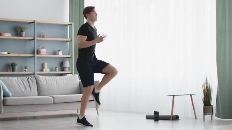 Man doing low impact high knees marching in living room as part of 15 minute home workout no jumping for beginners